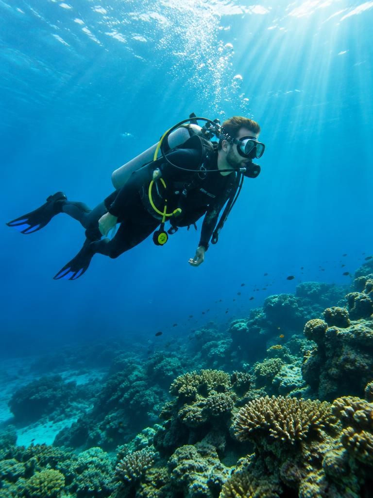 A scuba diver gliding over a coral reef in clear blue water.