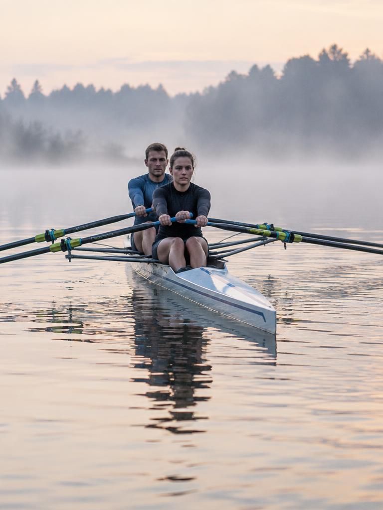 A woman and a man rowing a double scull on a misty lake at dawn.